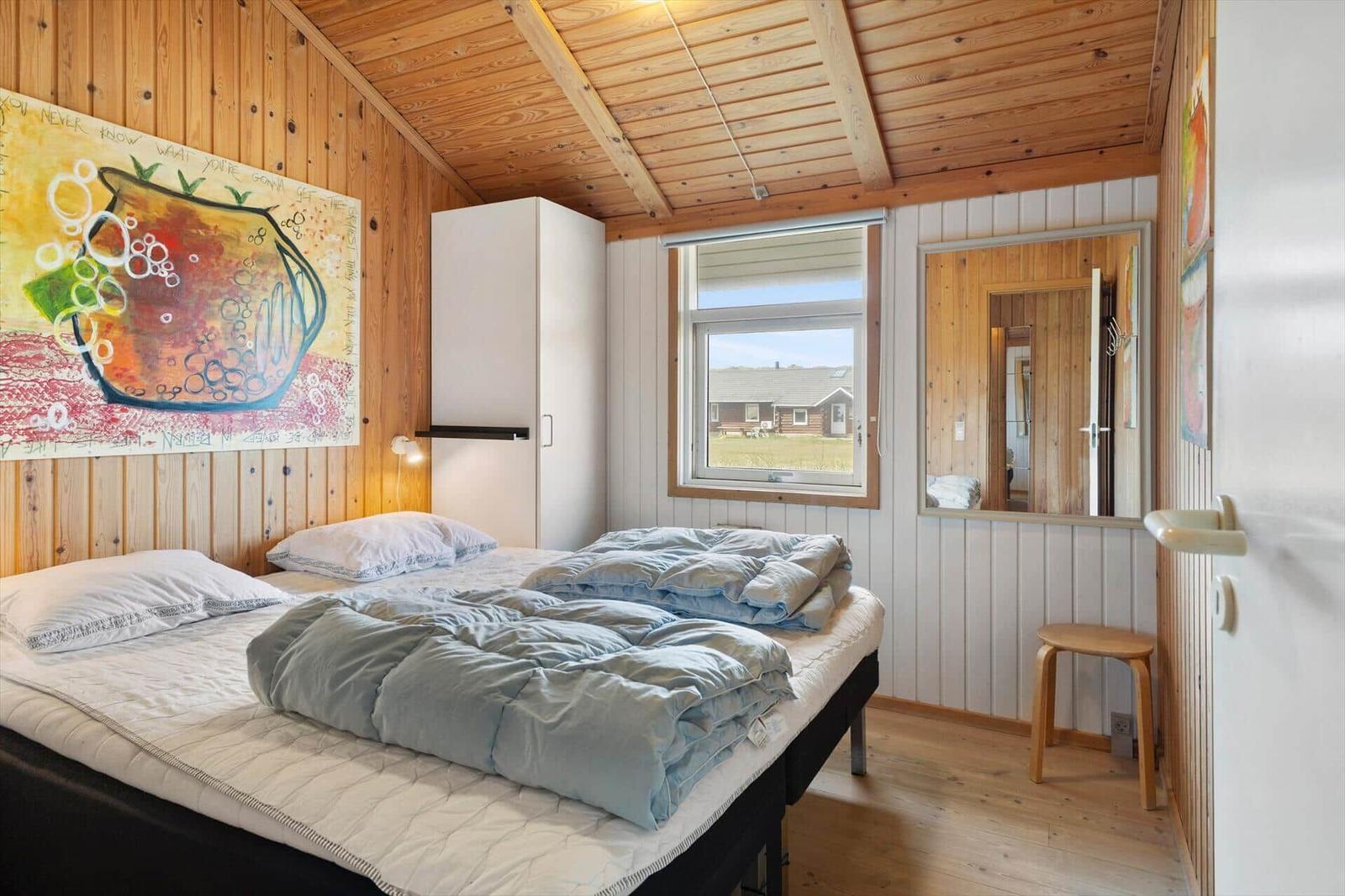 Schlafzimmer mit Holzwand, Bett, Fenster und Spiegel