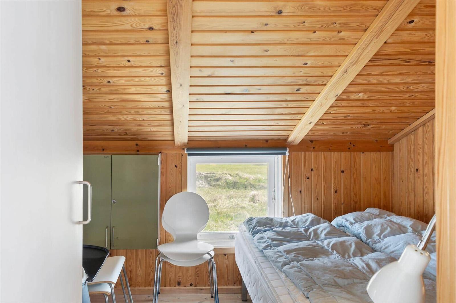 Schlafzimmer mit Holzwand, Bett, Stuhl und Fenster mit Blick auf Grasland.