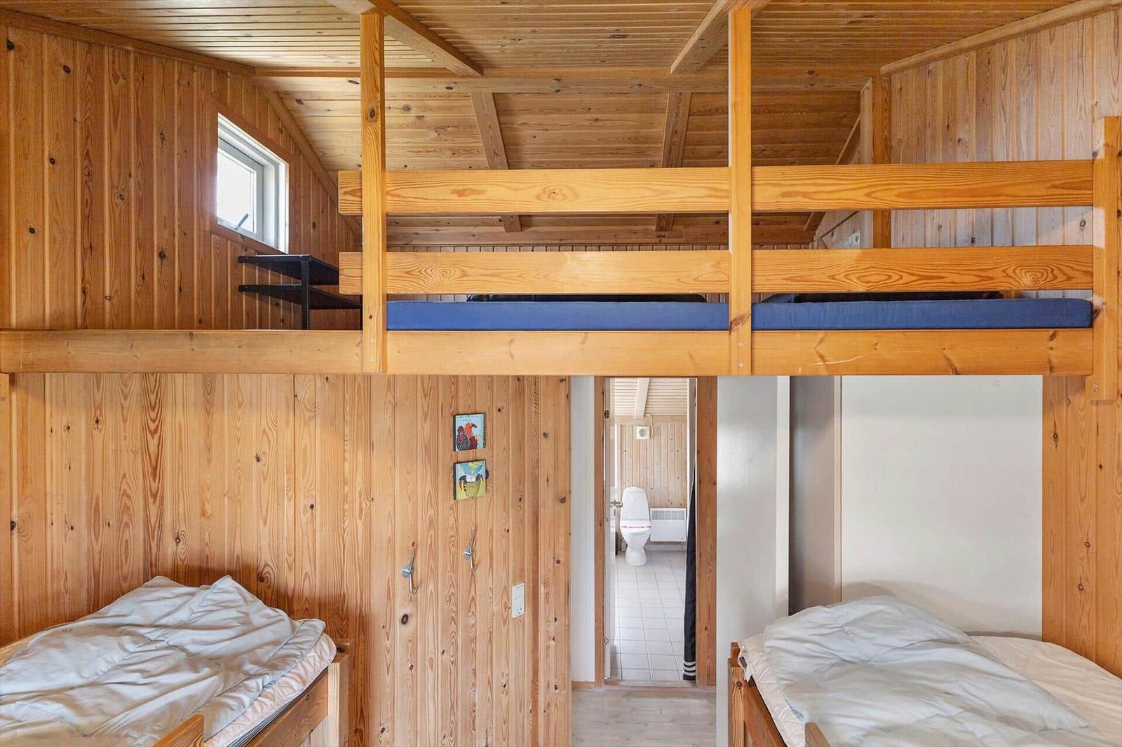 Zimmer mit Doppelstockbett und zwei Einzelbetten. Holzwände und Türöffnung zum Bad.