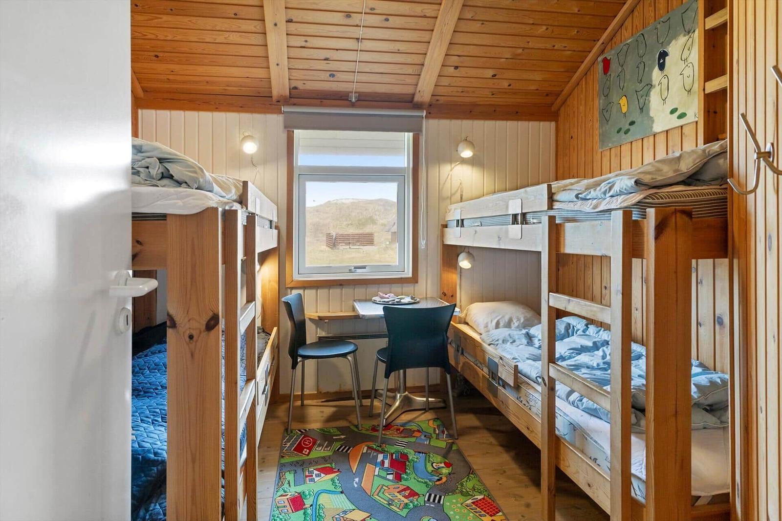 Zimmer mit zwei Etagenbetten, Tisch, Stühlen und Fensterblick auf Landschaft.