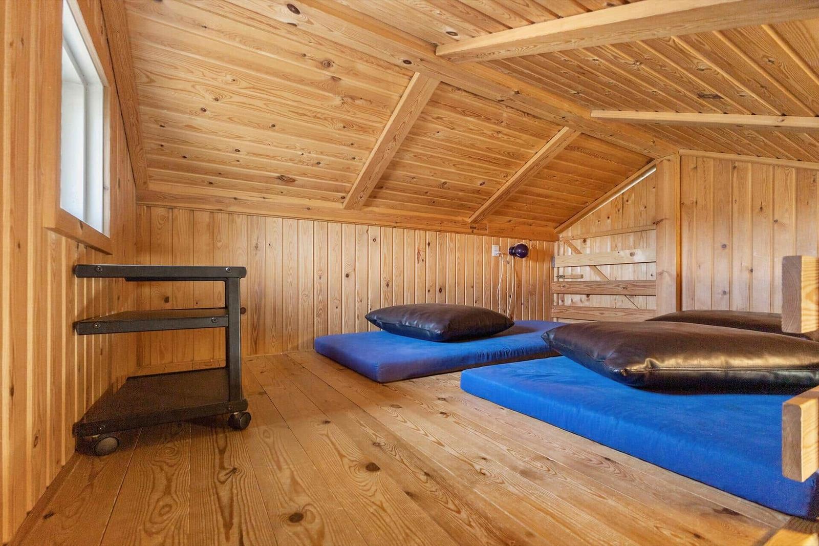 Zimmer mit Holzwand, Holzdecke und zwei blauen Matratzen mit Kissen.