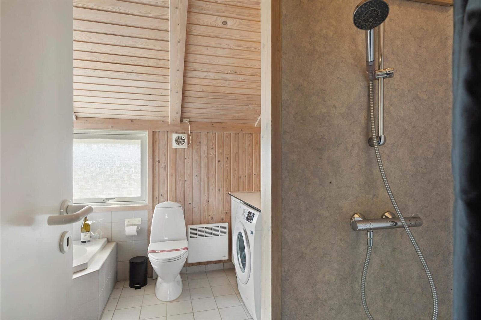 Bad mit Dusche, Toilette und Waschmaschine. Holzwände und Fenster.