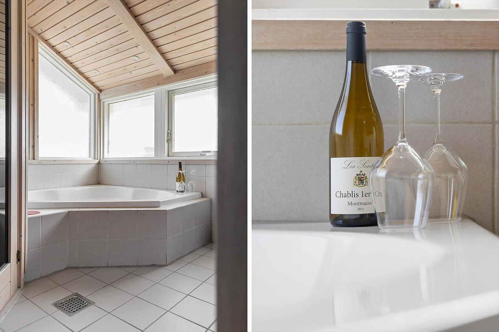 Bad mit Whirlpool und Fenstern. Weißer Tisch mit Weinflasche und Gläsern.