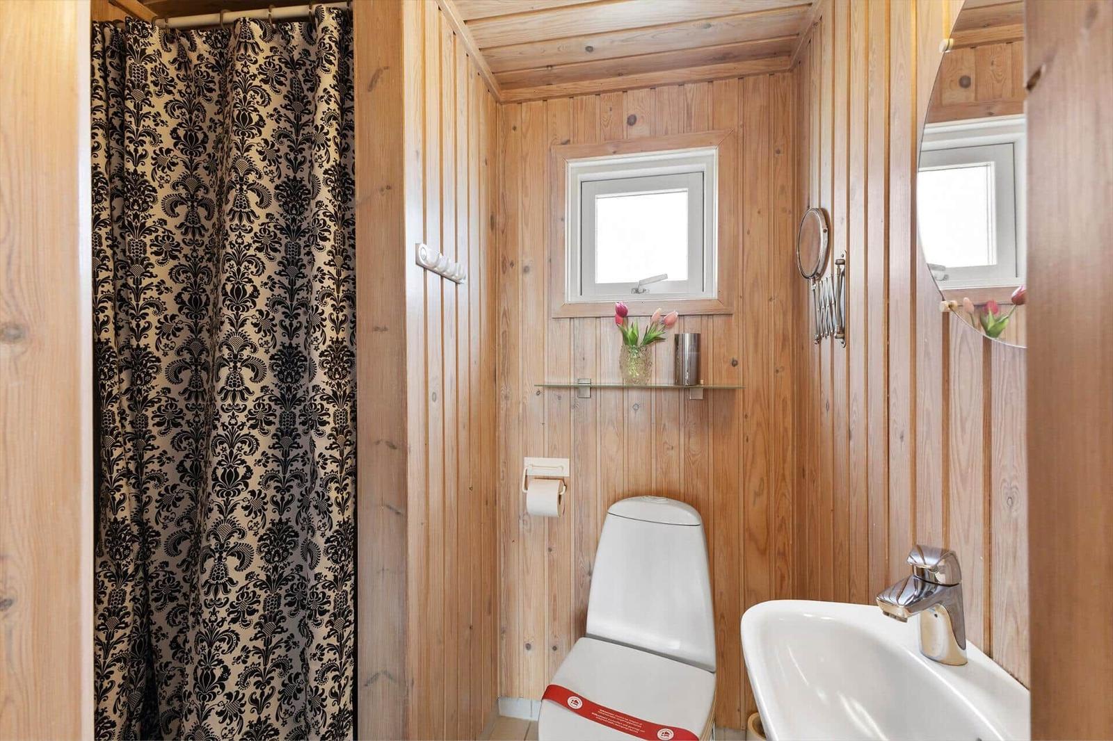 Badezimmer mit Holzwand, Toilette, Waschbecken und Duschvorhang mit Muster.