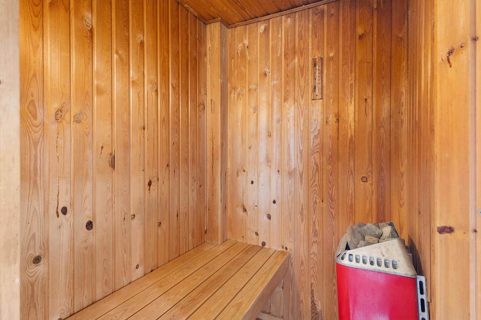 Sauna mit Holzwand und Sitzbank. Holzkiste mit Steinen steht rechts.