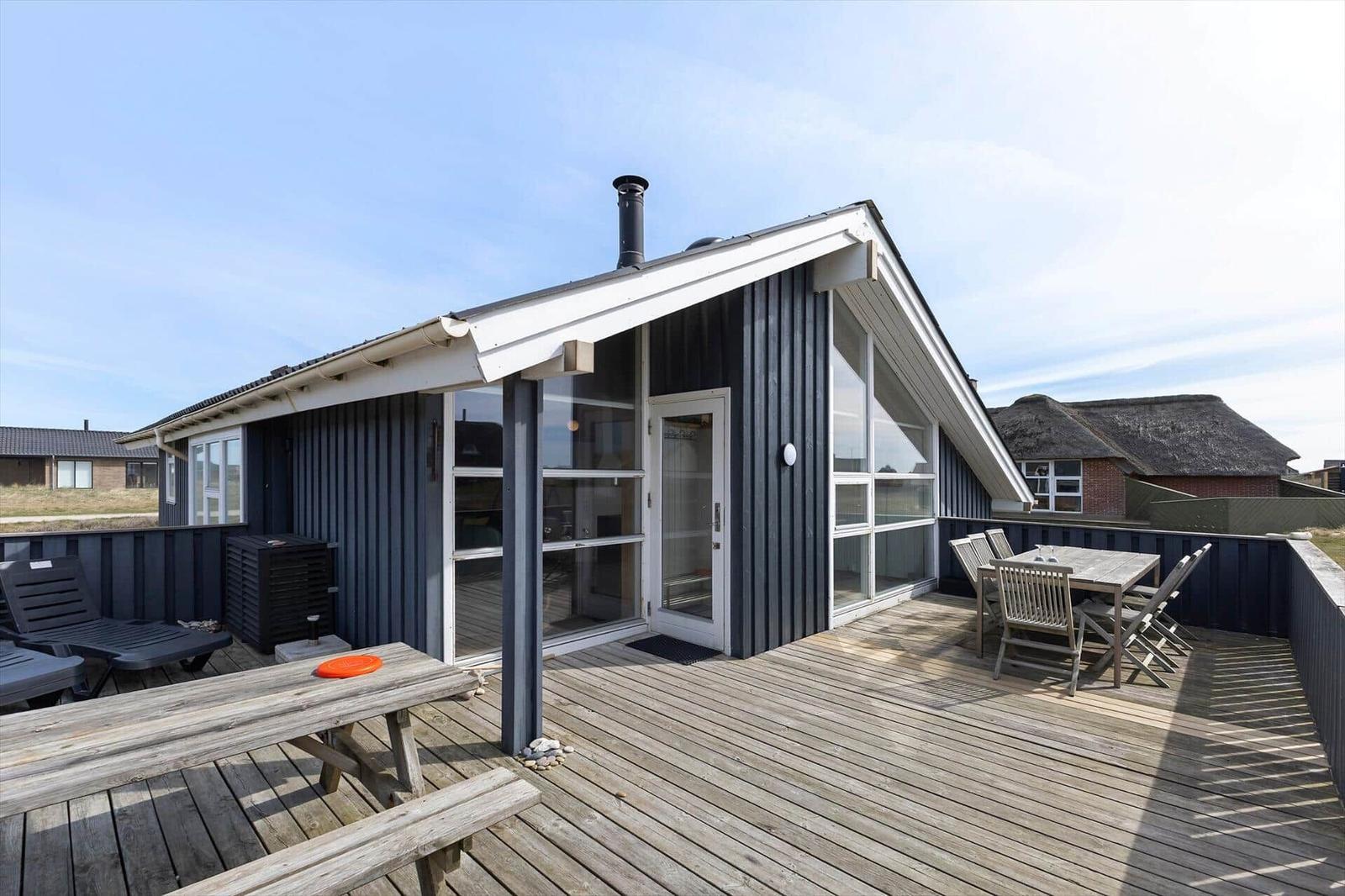 Moderne Strandhütte mit großem Holzterrasse, Sitzgelegenheiten und Blick auf das Meer.