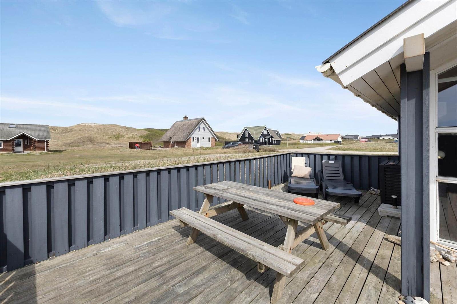 Terrasse mit Picknicktisch, Liegestühlen und Blick auf Strandhäuser.