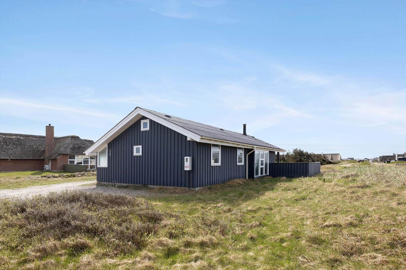 Ein modernes Haus mit dunkler Fassade und weißen Fensterrahmen in einer grünen Landschaft.