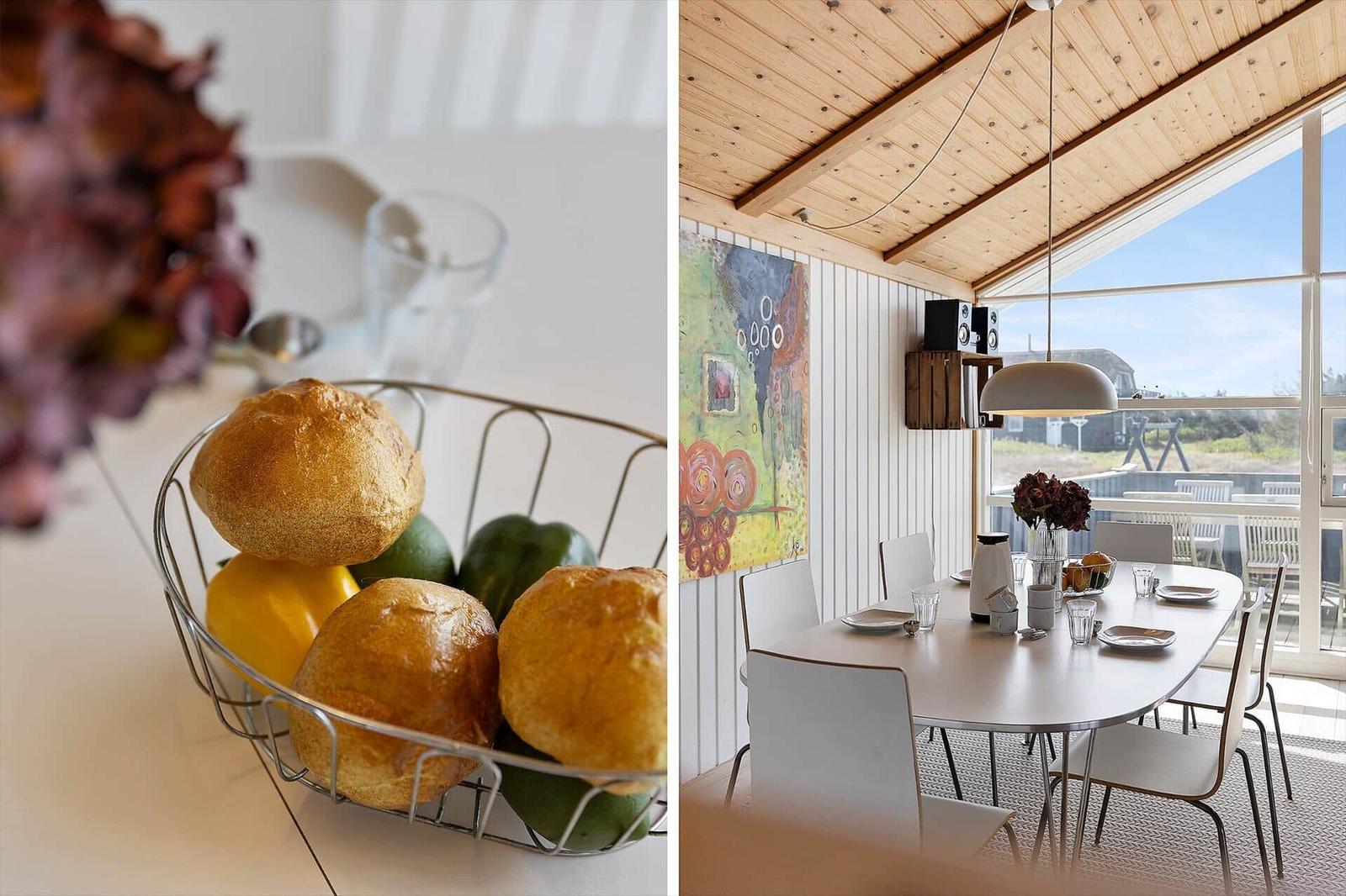 Esszimmer mit Holzdecke und großem Fenster. Tisch mit Stühlen und Obstschale.