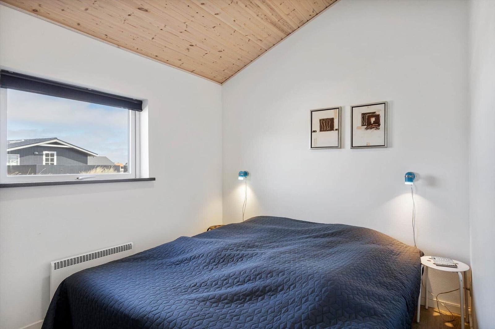 Schlafzimmer mit blauem Bett, Holzdecke und Fensterblick auf Haus