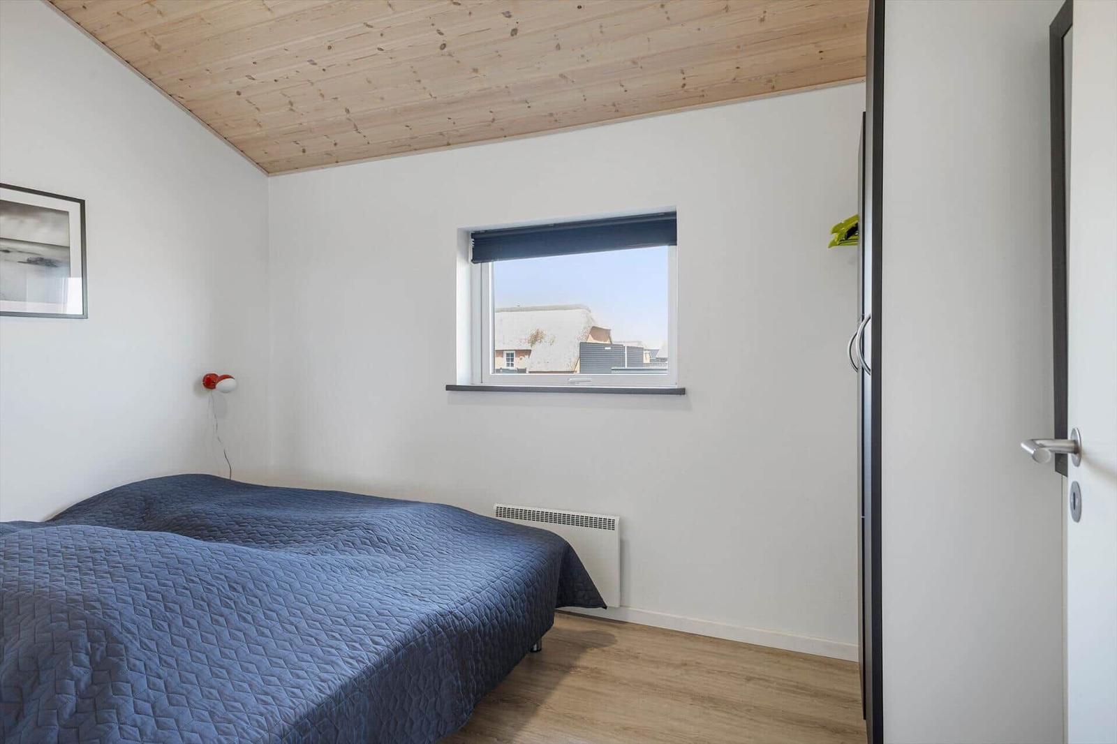 Schlafzimmer mit Bett, Fenster und Holzdecke.