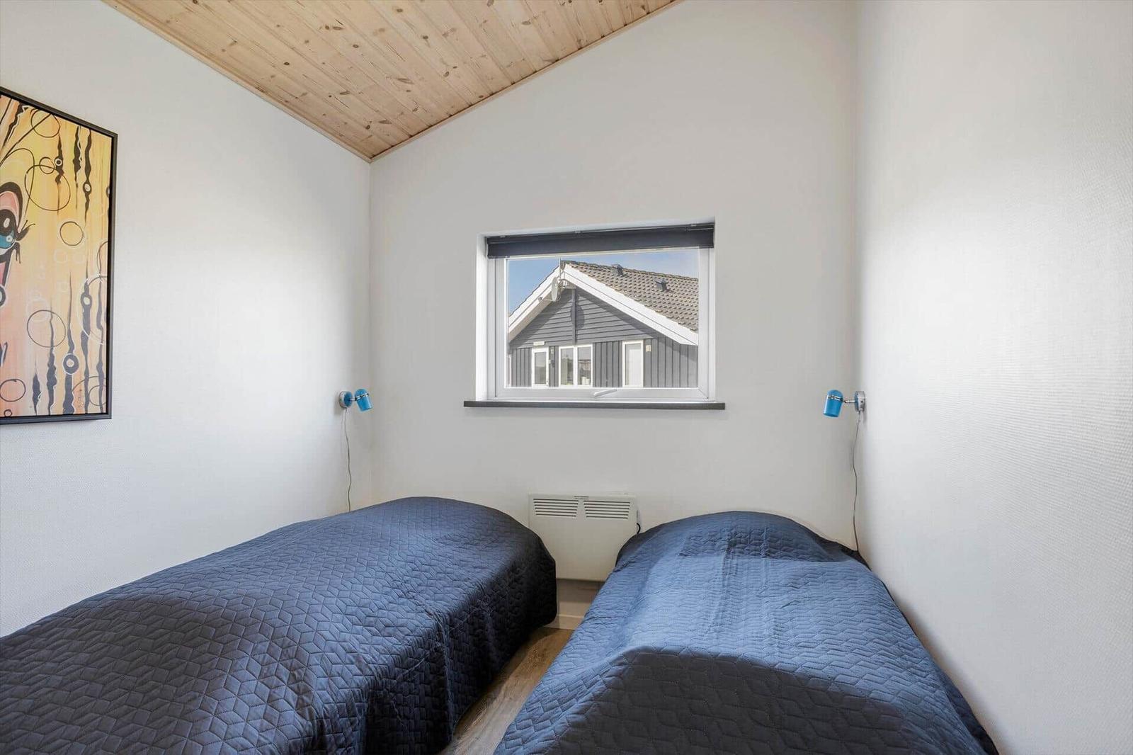 Zwei Betten mit blauen Bettdecken, Wandbild und Fenster mit Blick auf ein Haus.
