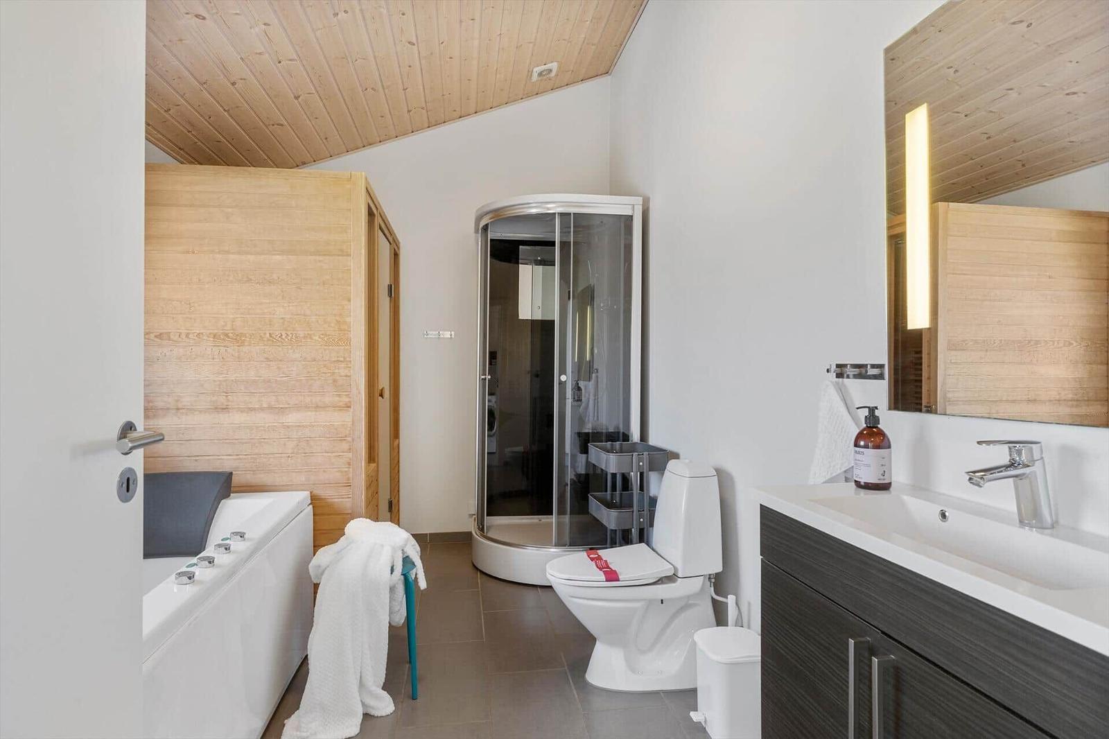 Badezimmer mit Dusche, Toilette und Waschbecken. Holzdecke und -wände.