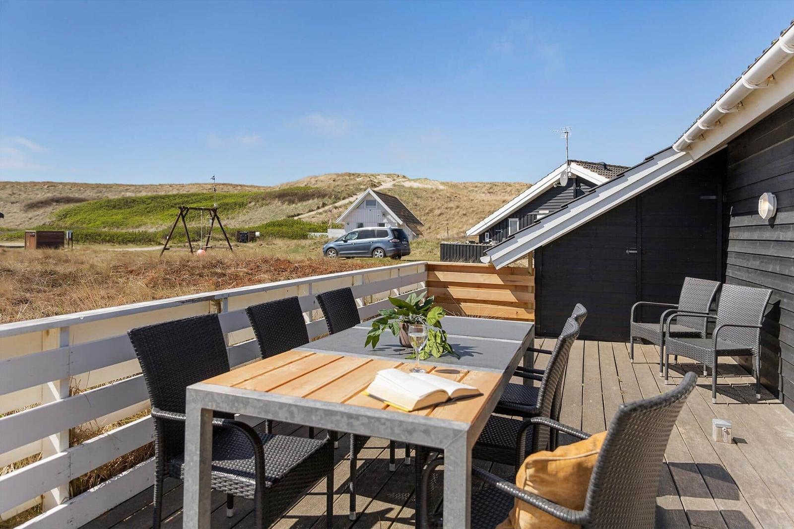 Terrasse mit Tisch und Stühlen, Blick auf Dünen und Haus.