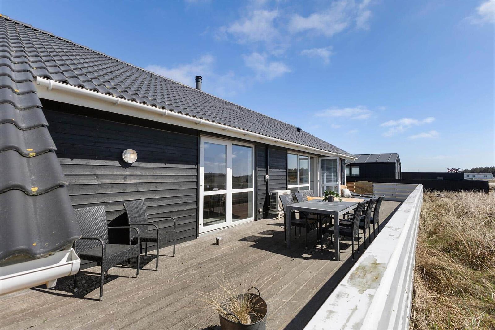 Terrasse mit Tisch und Stühlen vor einem Haus mit dunkler Fassade und Glasfenstern.