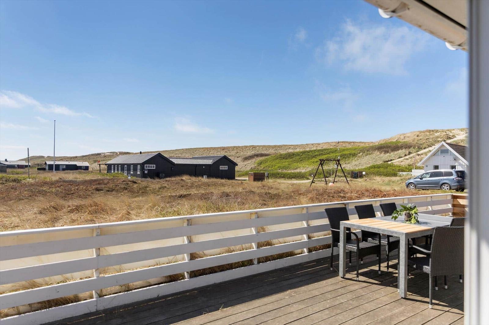 Terrasse mit Tisch und Stühlen. Blick auf Dünensand und Häuser.