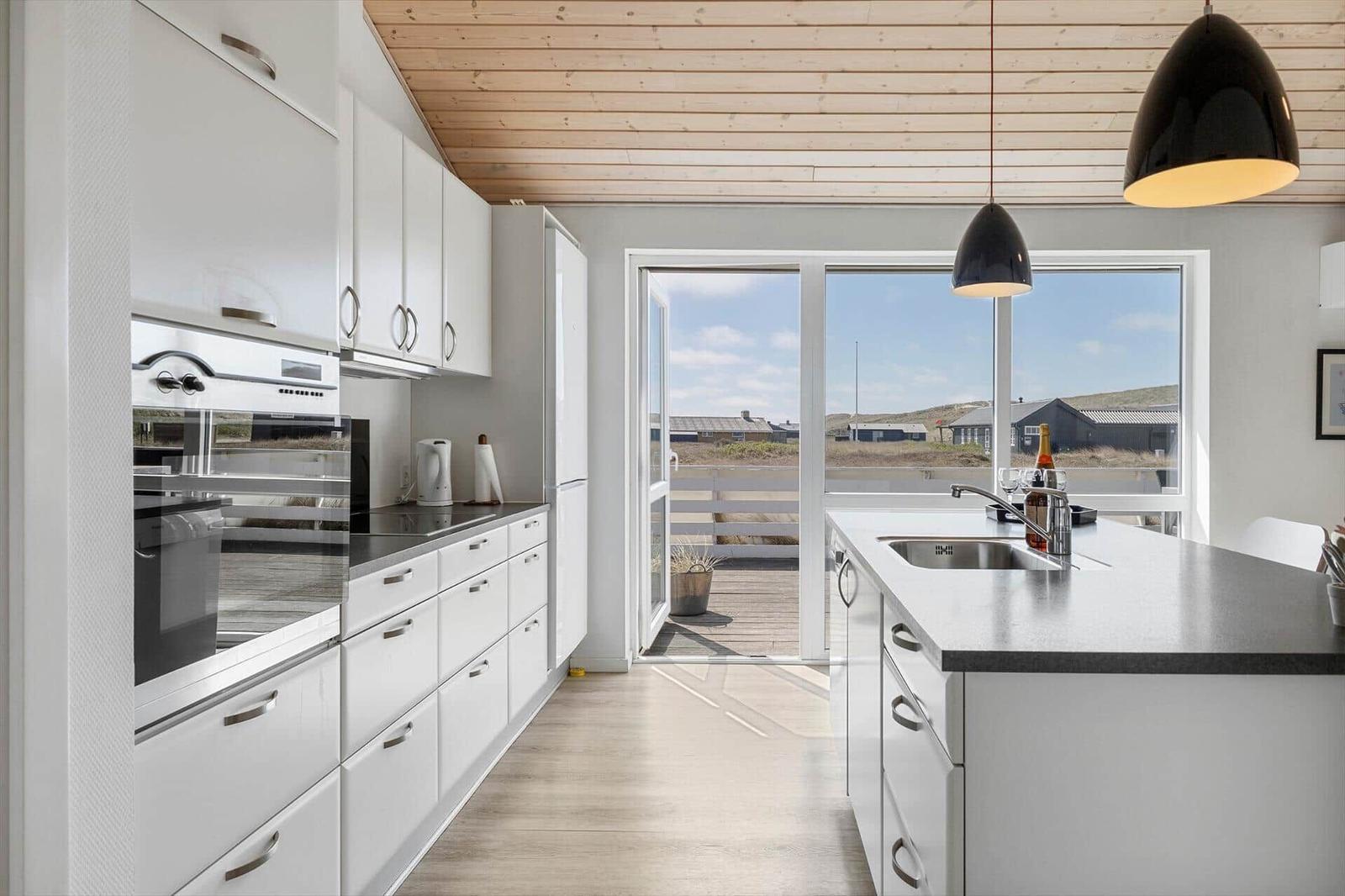 Moderne Küche mit weißen Schränken, Steinplatte und Blick auf Terrasse.