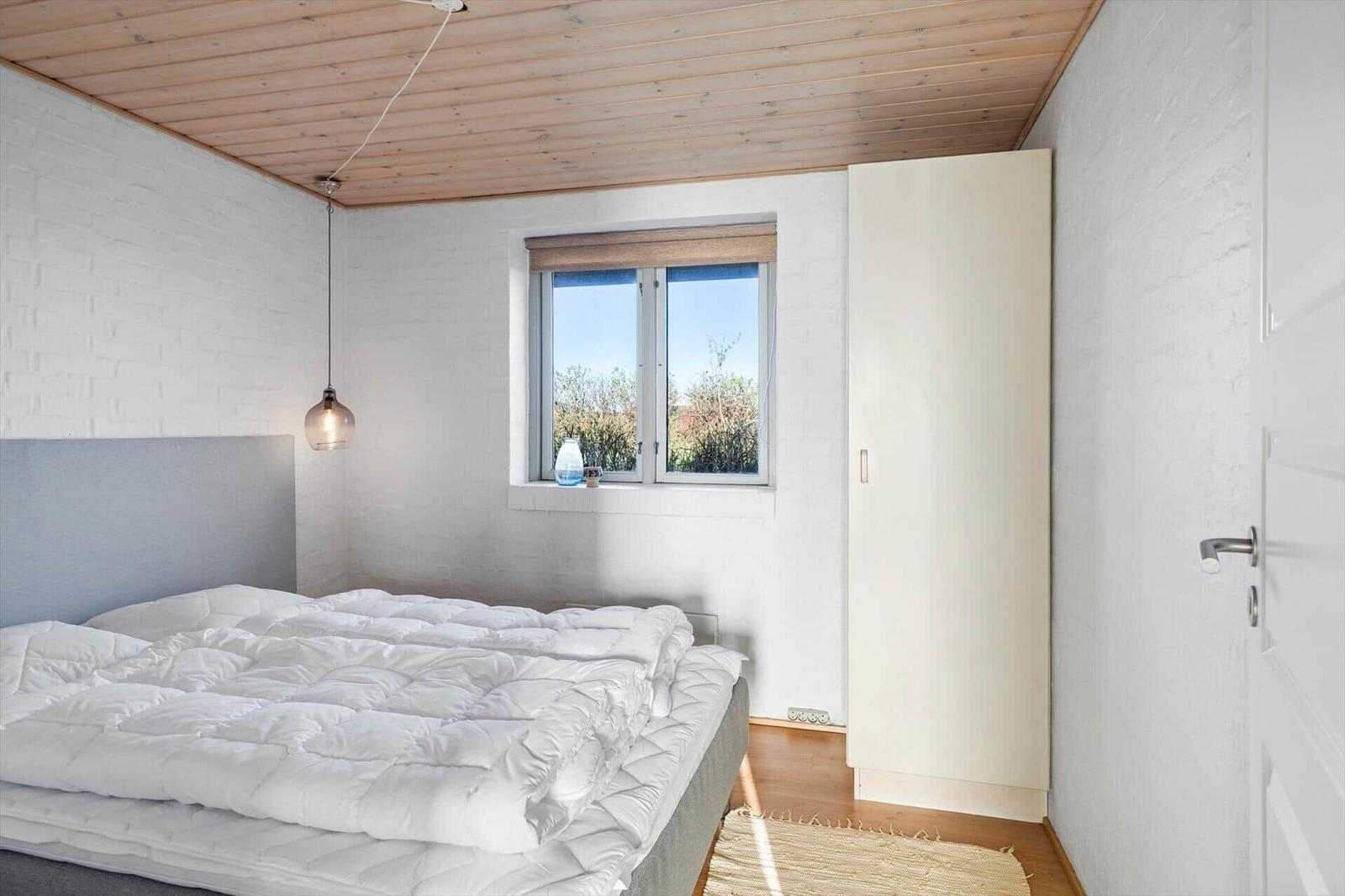 Schlafzimmer mit Bett, Fenster und Kleiderschrank.