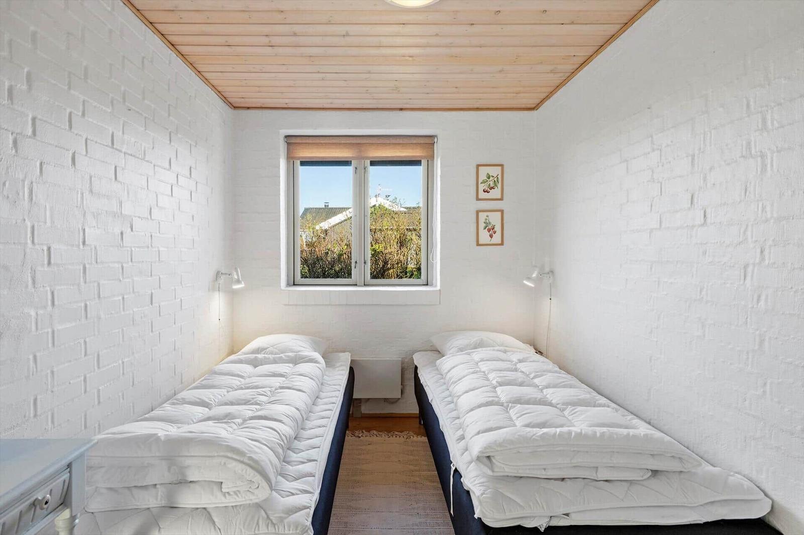 Zwei Schlafplätze mit Matratzen und weißen Decken. Fenster mit Blick nach draußen.