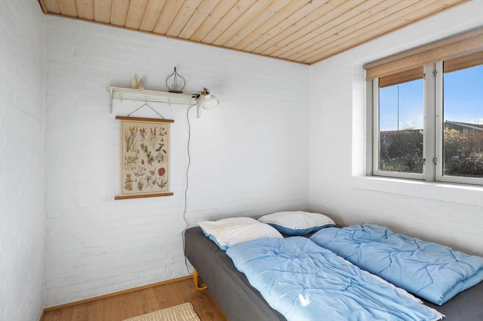 Schlafzimmer mit Bett, Fenster und Wandbild. Holzdecke und weiße Wände.