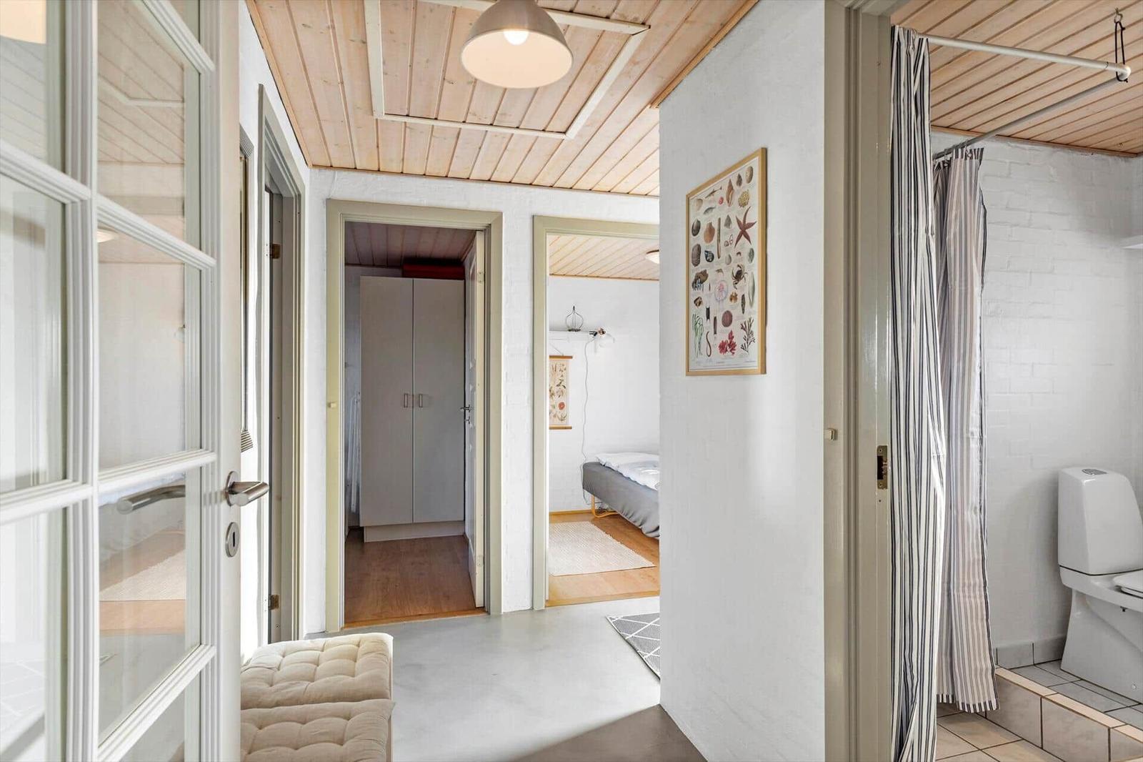 Flur mit Schlafzimmer und Bad. Holzdecke, weiße Wände und Tür. Wandbild mit Meereslebewesen.