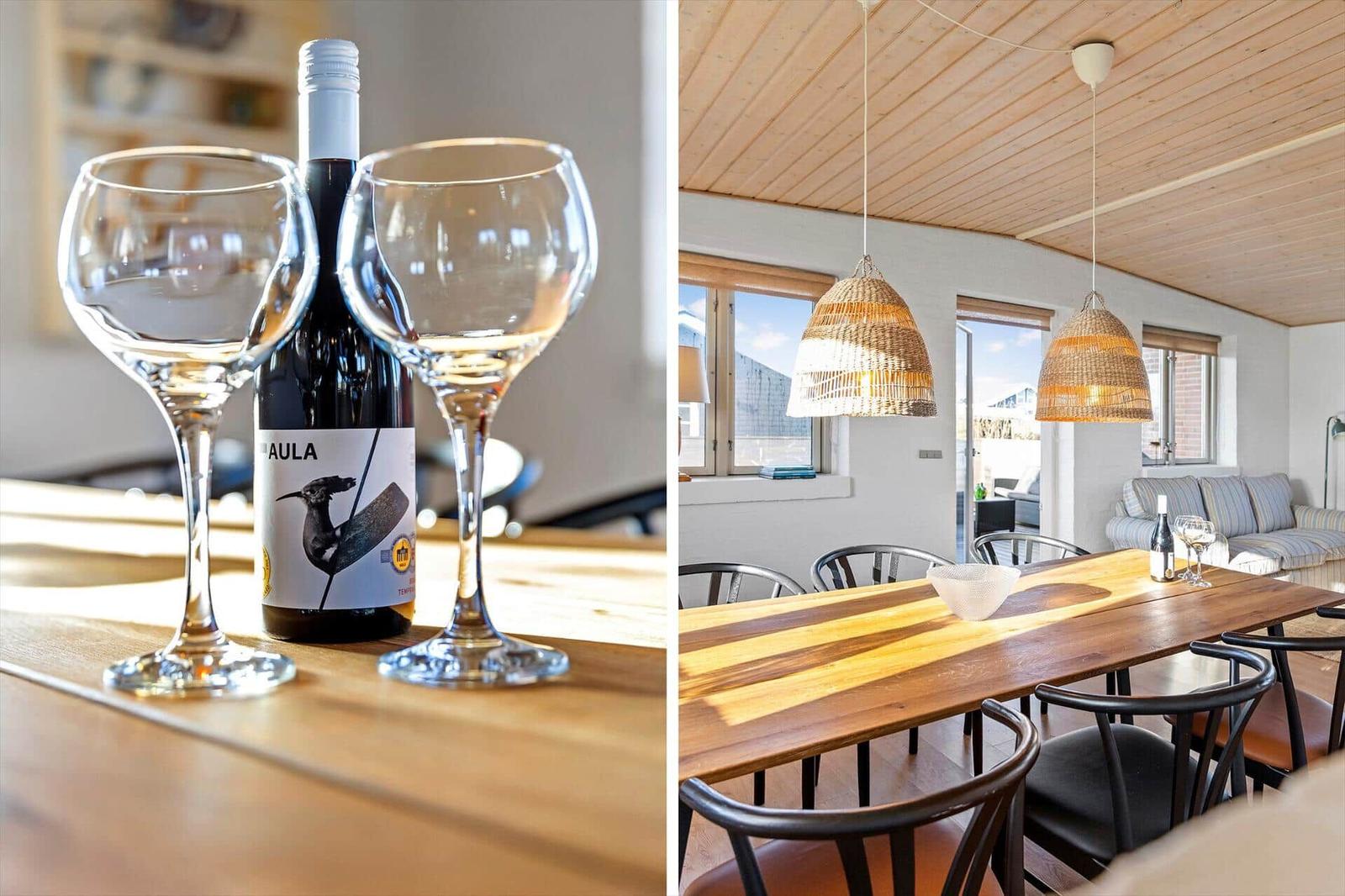 Tisch mit Weinflasche und Gläsern. Esszimmer mit Holztisch, Stühlen und Hängelampen.