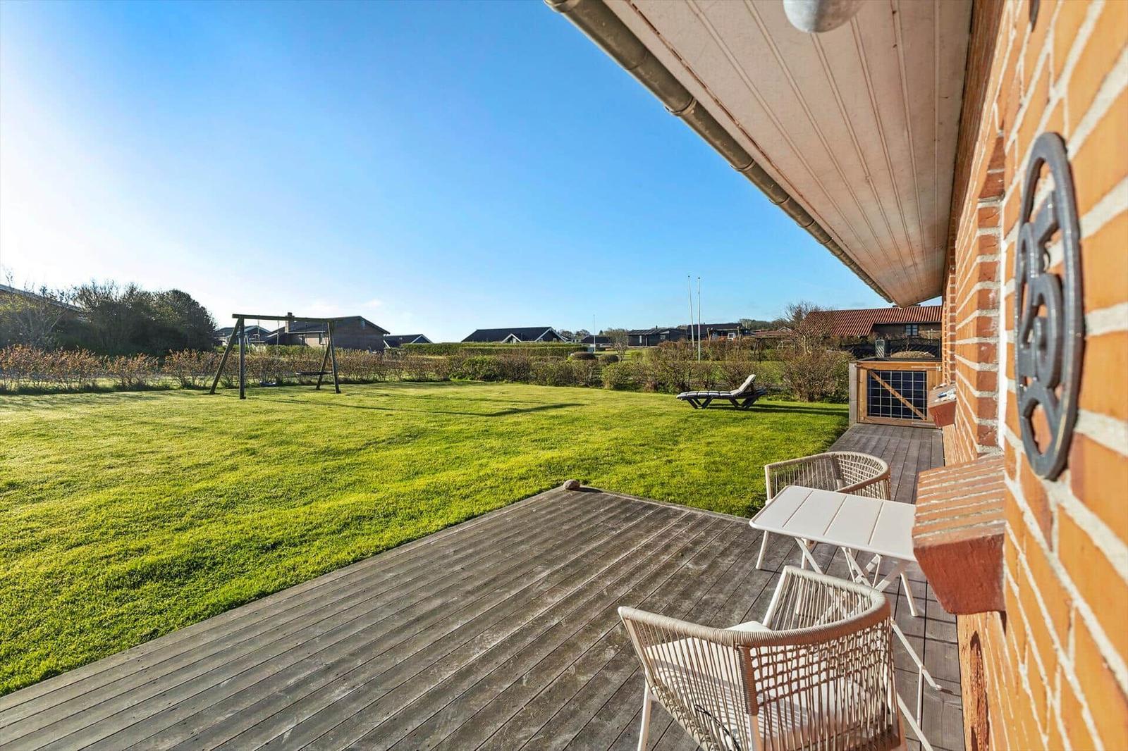 Terrasse mit Tisch und Stühlen, Blick auf grünen Garten mit Schaukel und Liegestuhl.