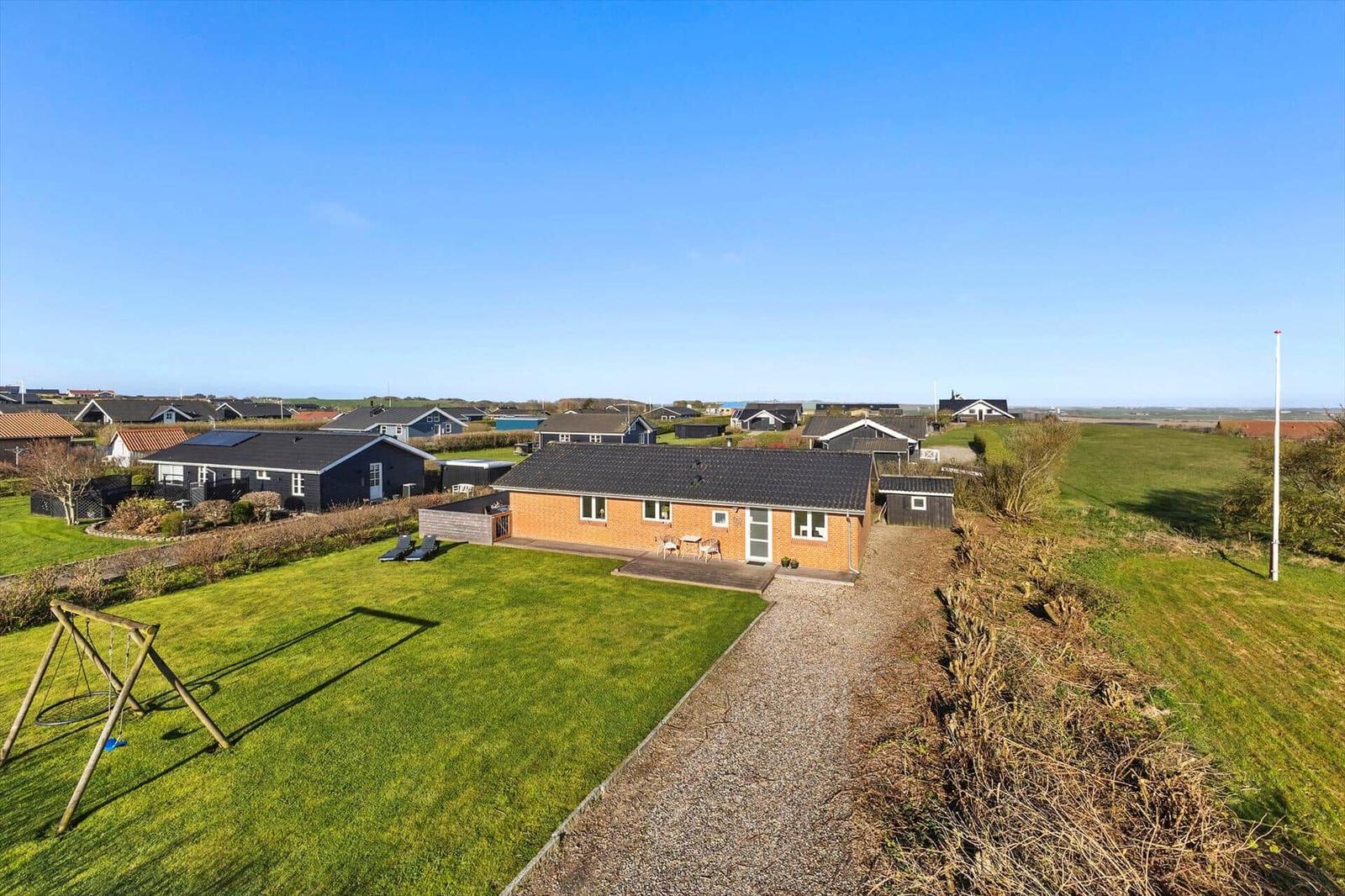 Ein Haus mit Garten, Spielplatz und Terrasse. Im Hintergrund sind weitere Häuser und Felder.