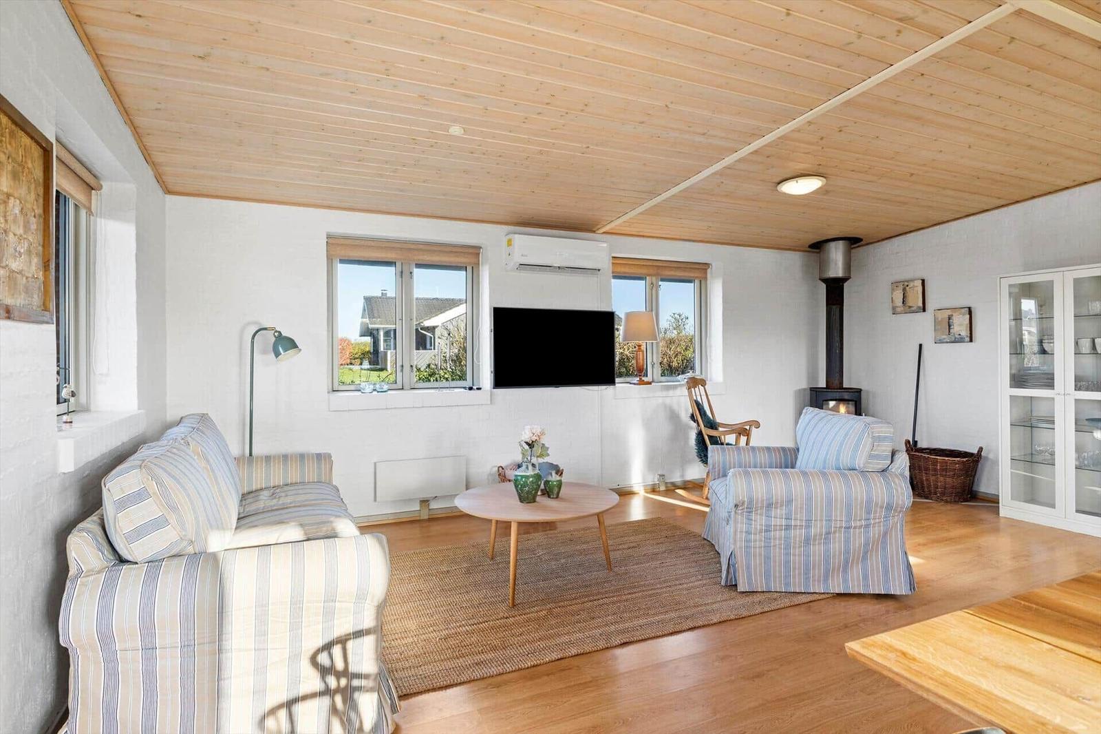 Wohnzimmer mit Sofa, Sessel, Couchtisch und Kaminofen. Holzdecke und Fenster mit Blick.