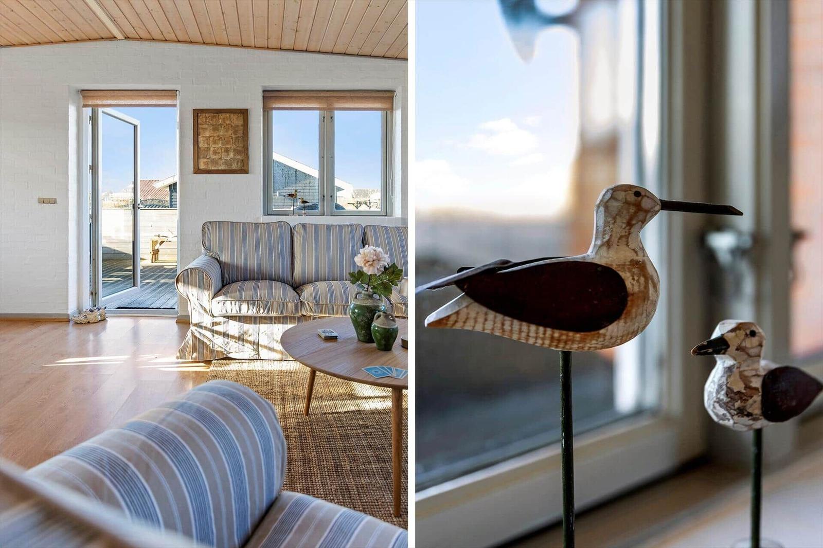 Wohnzimmer mit Sofa, Tisch und Fenstern. Holzvogeldekoration vor Fenster.