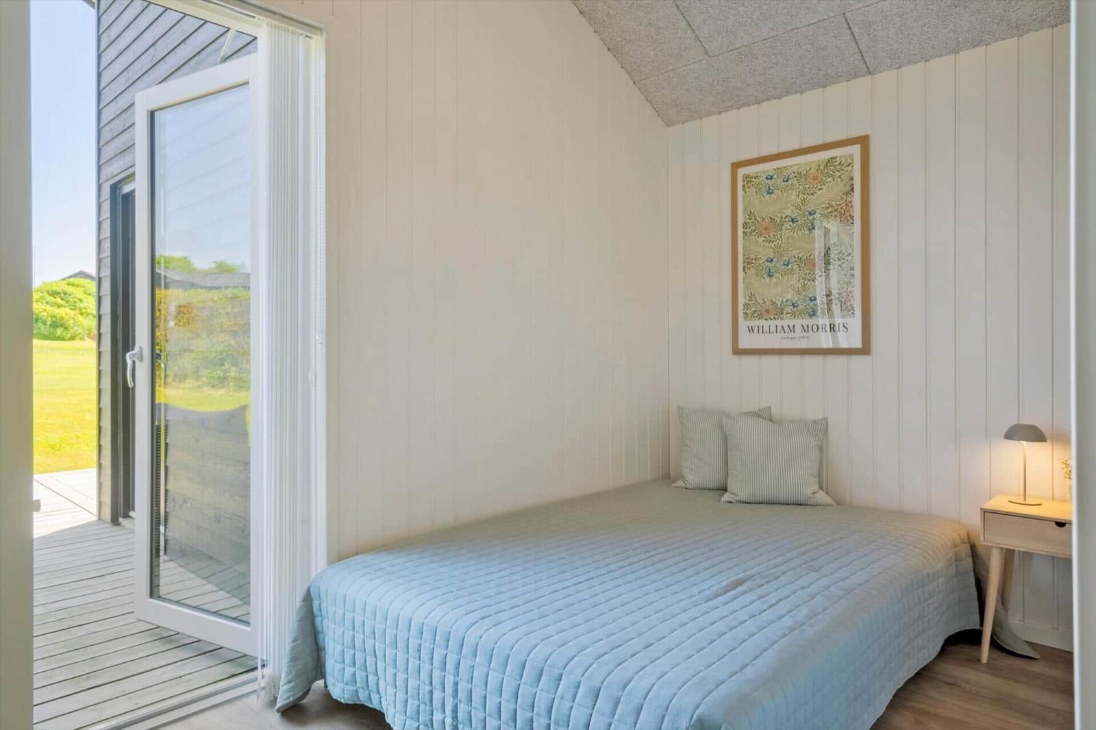Schlafzimmer mit Bett, Bild an der Wand und Glastür zum Balkon.