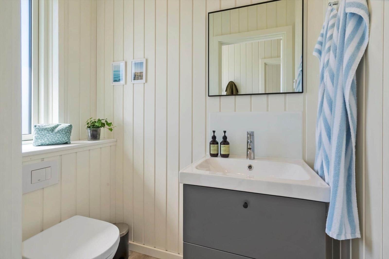 Badezimmer mit Waschbecken, Spiegel, Toilette und Fenster mit Pflanze.