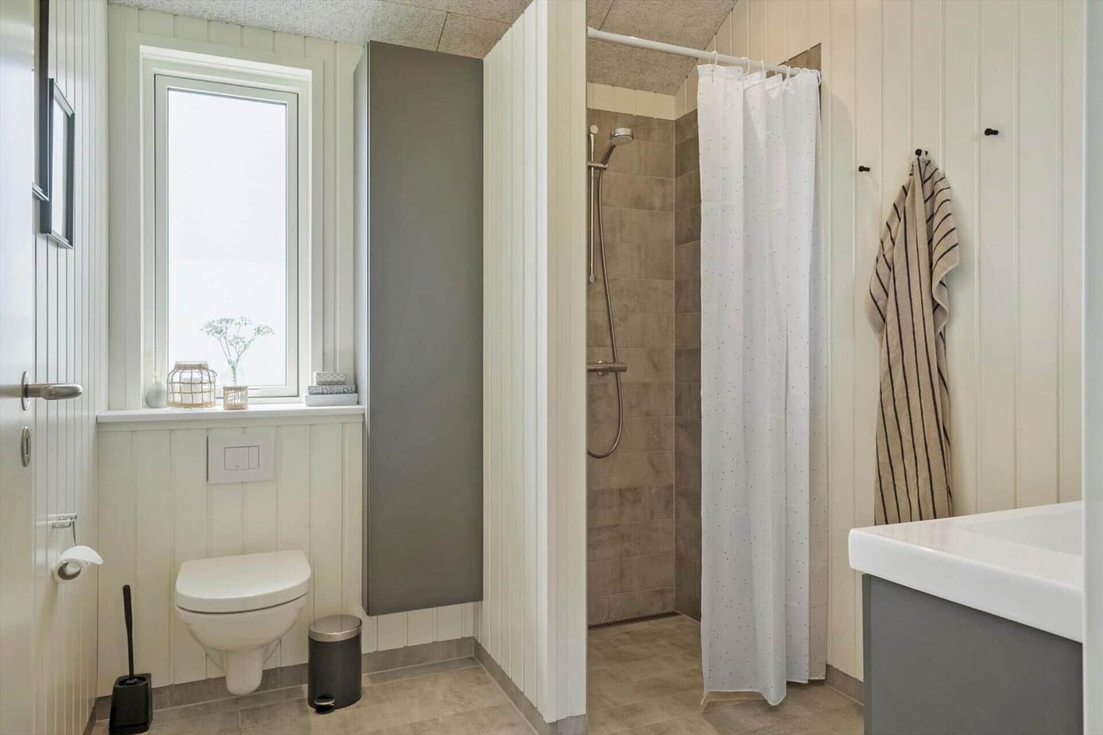 Badezimmer mit Dusche, Toilette und Waschbecken. Fenster mit Blumendekor.