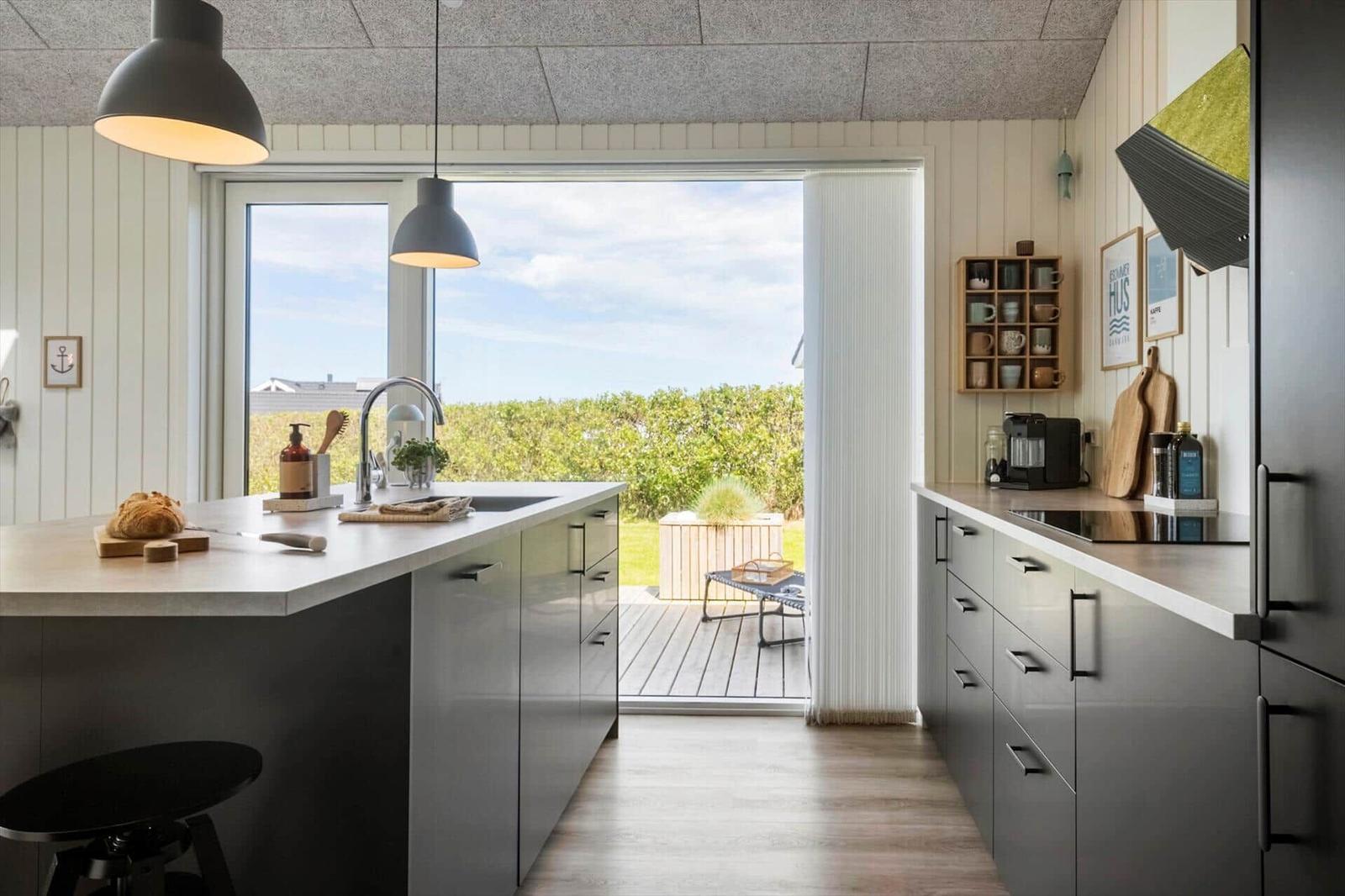 Küche mit Blick auf Terrasse und Grünfläche. Moderne Einbauküche und Kücheninsel.