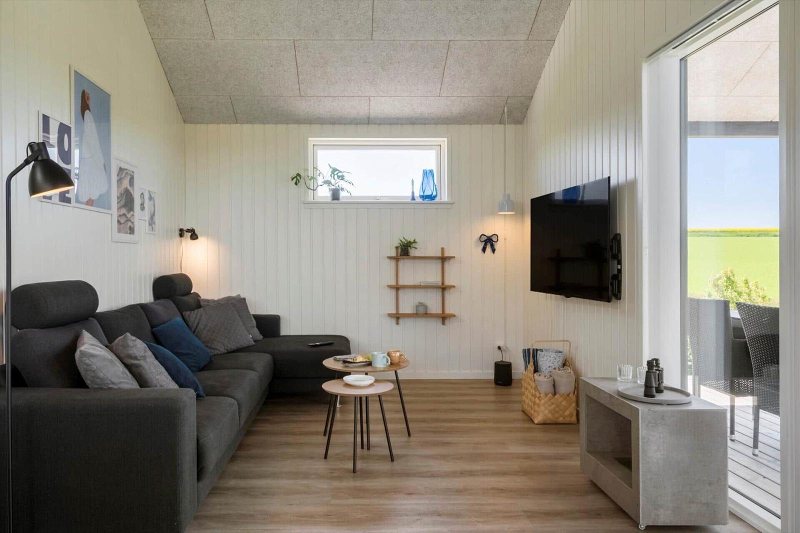 Wohnzimmer mit Sofa, TV und Terrasse mit Blick auf Feld