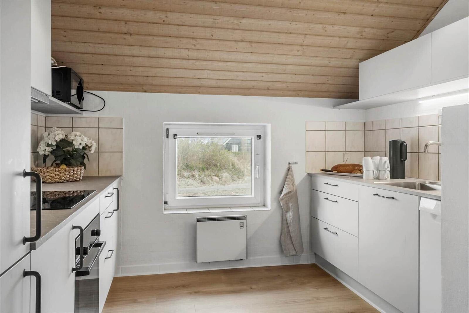 Küche mit weißen Schränken, Holzdecke und Fenster zur Außensicht.