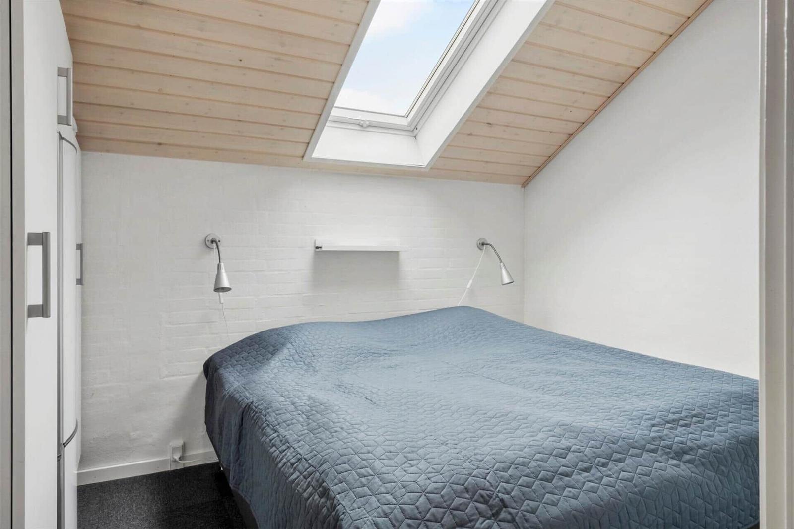 Schlafzimmer mit Dachfenster, Bett und Wandlampen.