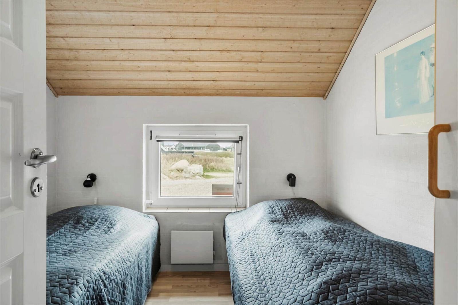 Zwei Betten mit blauen Bettdecken unter einem Holzdecken, ein Fenster und eine Wanddekoration.