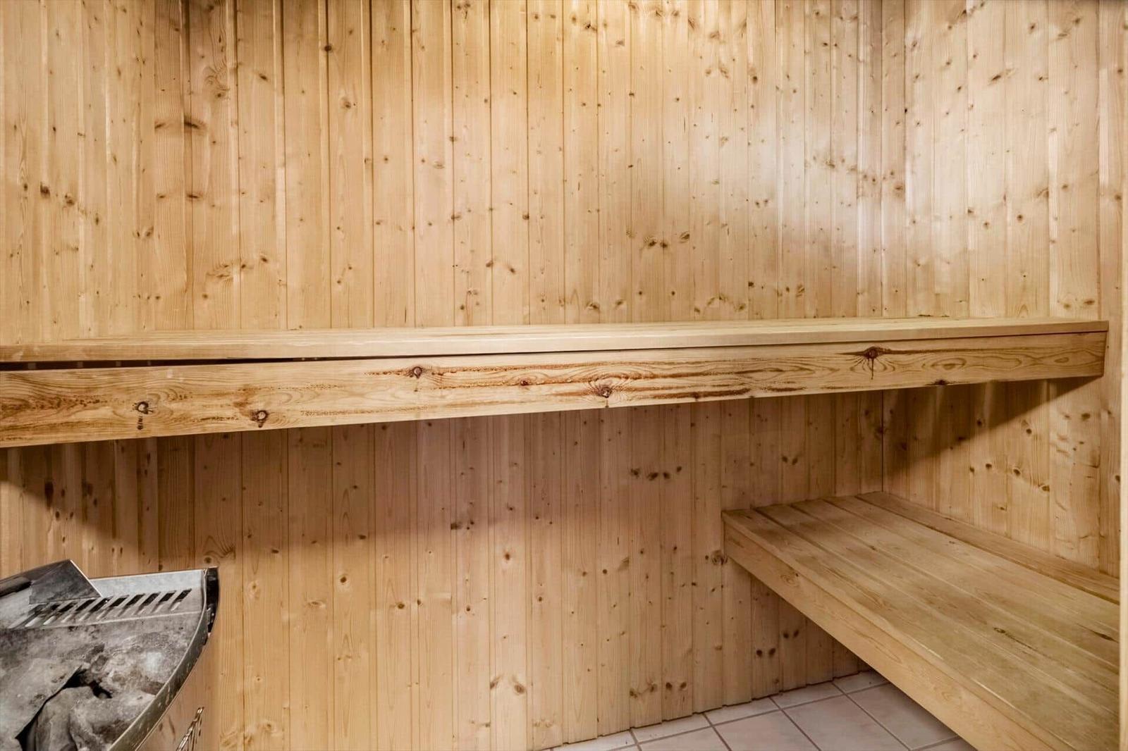 Sauna mit Holzwand und Sitzbänken. Links ist ein Ofen sichtbar.