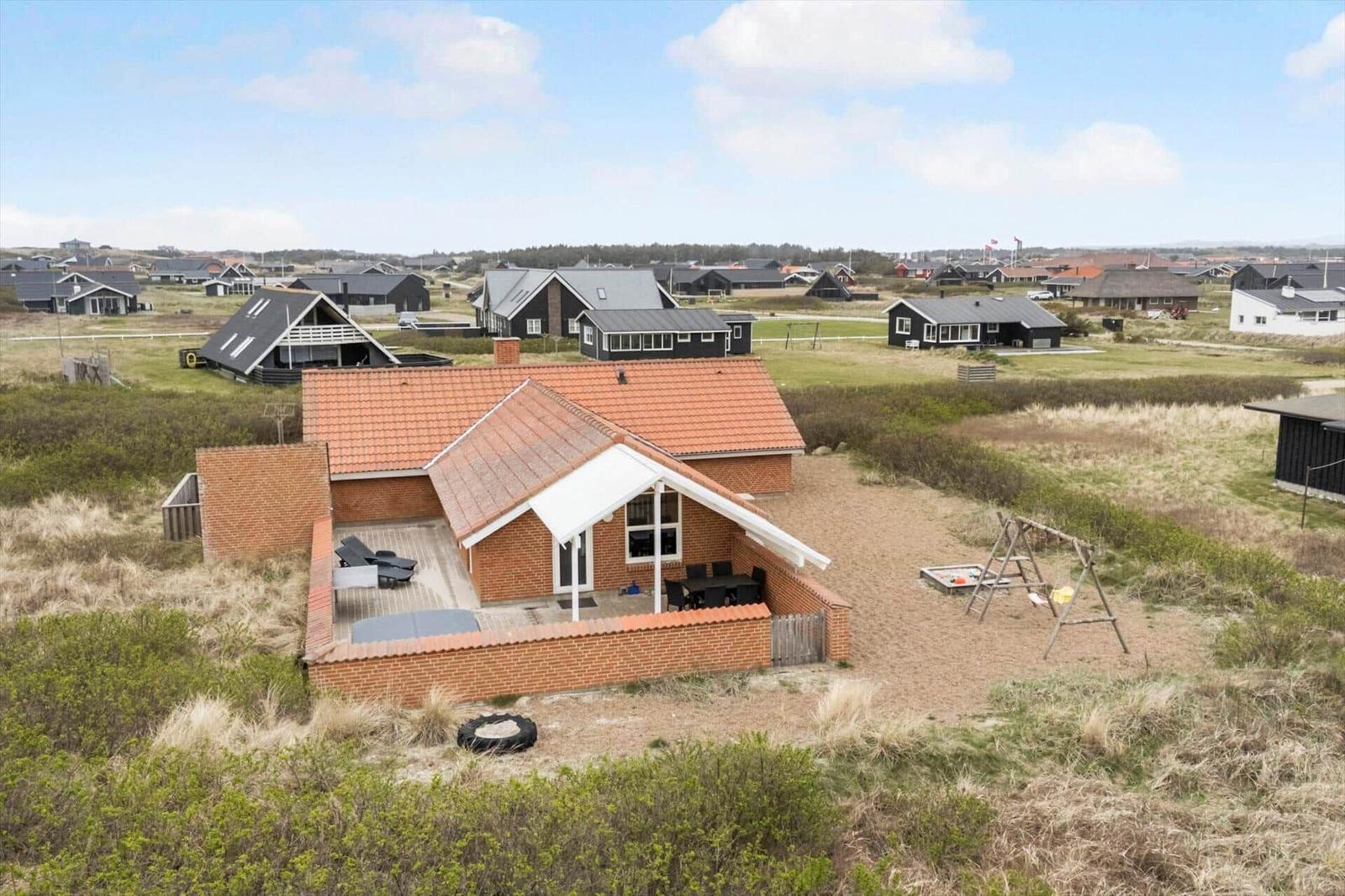 Ein Haus mit rotem Dach und Terrasse, umgeben von Gras und weiteren Häusern.