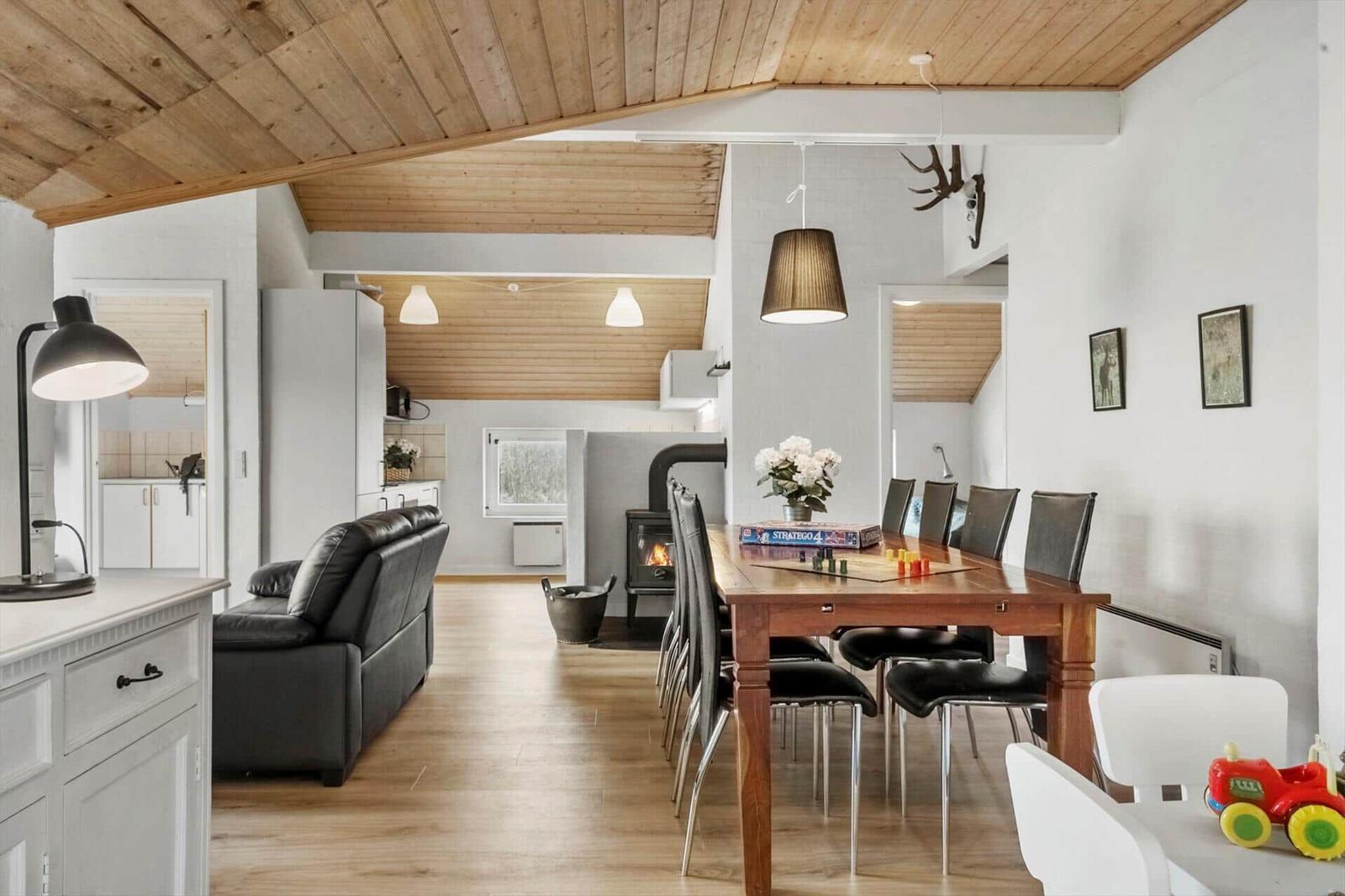 Wohn- und Essbereich mit Holzdecke, Esstisch, Sofa und Kaminofen.