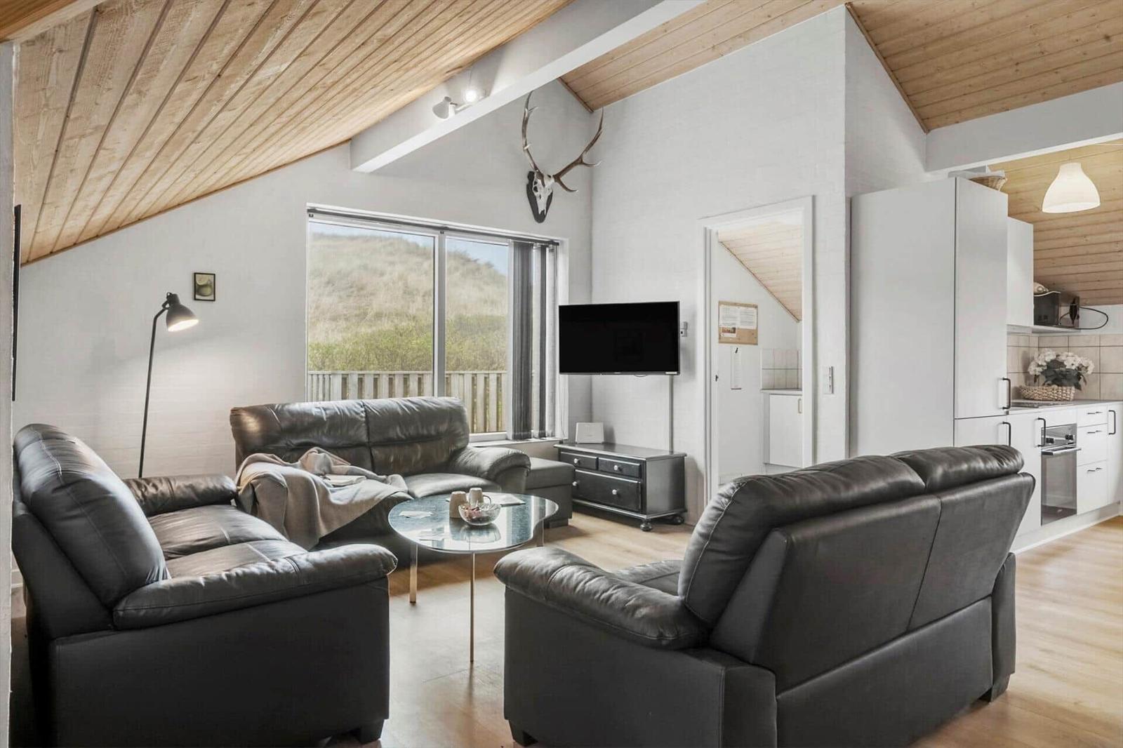 Wohnbereich mit zwei Ledersofas, TV und Blick auf die Außenterrasse.