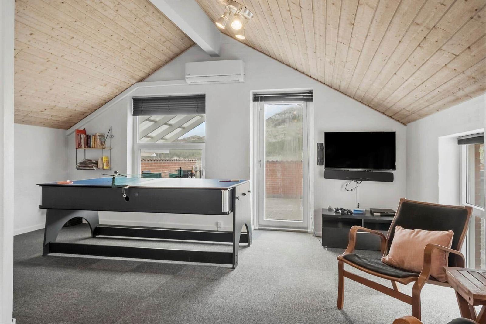 Raum mit Billardtisch, Fernseher und Sessel unter Holzdecke.