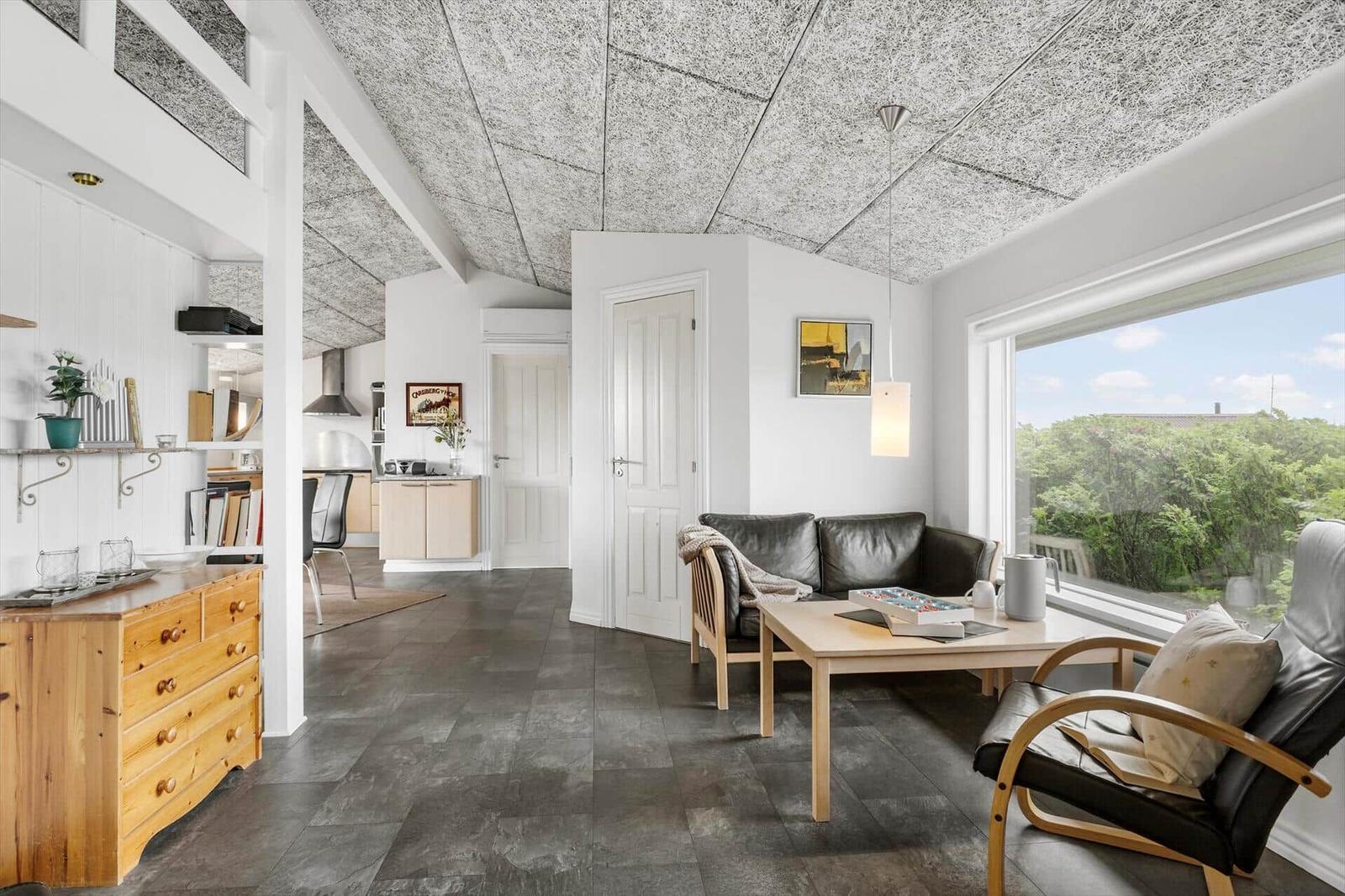 Wohnbereich mit Sofa, Sessel und Tisch. Große Fenster und dunkler Boden. Decke mit Textur.