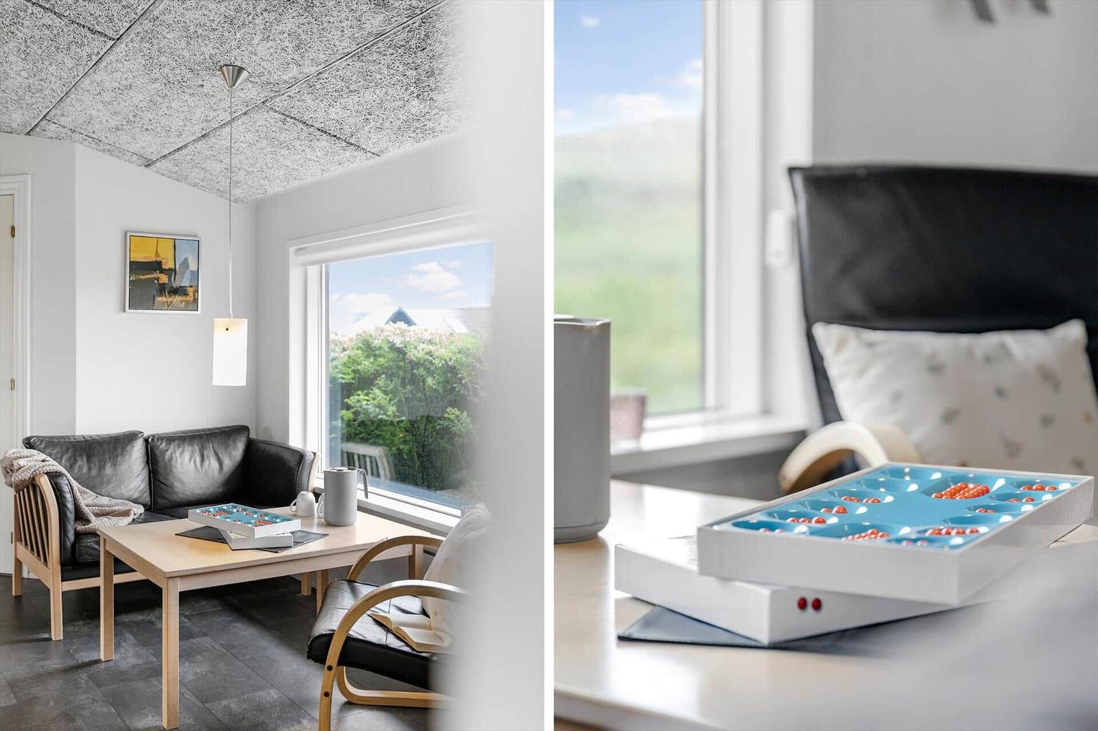 Wohnzimmer mit Sofa, Tisch und Blick auf grüne Landschaft. Nebenraum mit Schreibtisch und Spielbox.