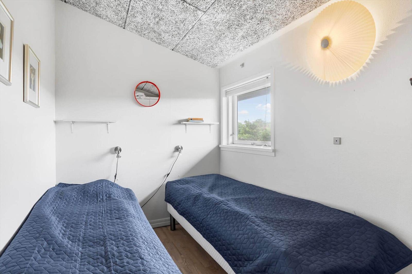 Zwei Betten mit blauen Bettdecken, Fenster, Wandspiegel und Deckenleuchte.