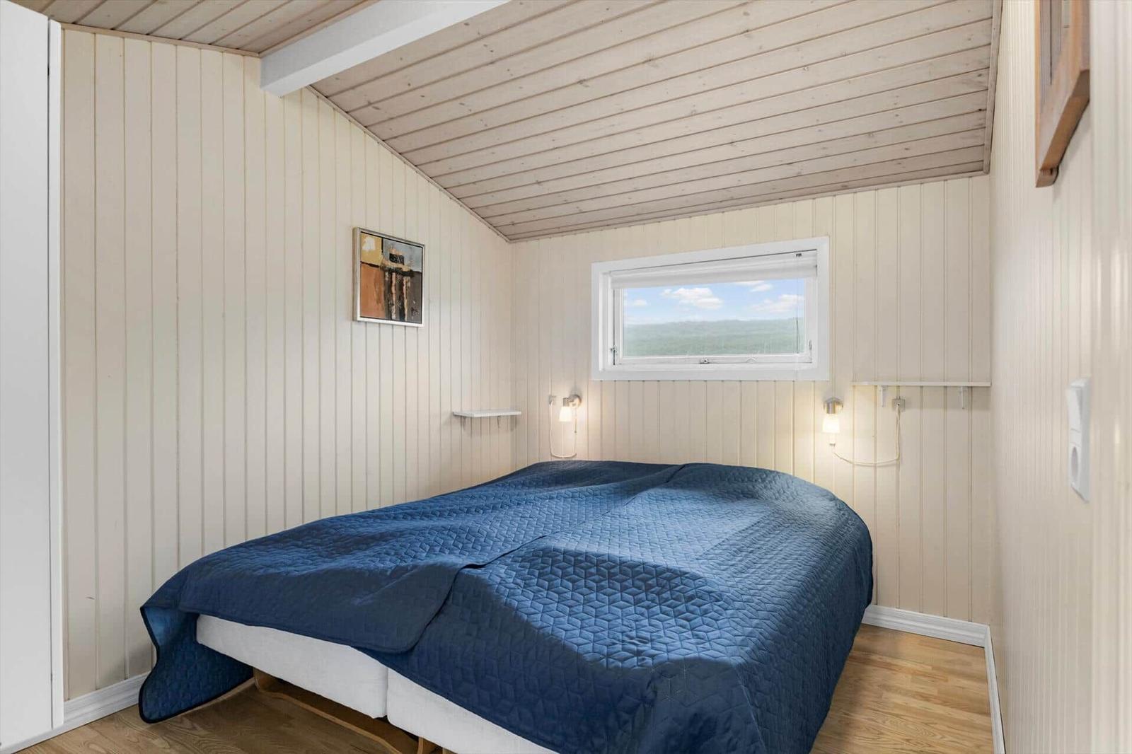 Schlafzimmer mit Bett, Fenster und Holzwandverkleidung.