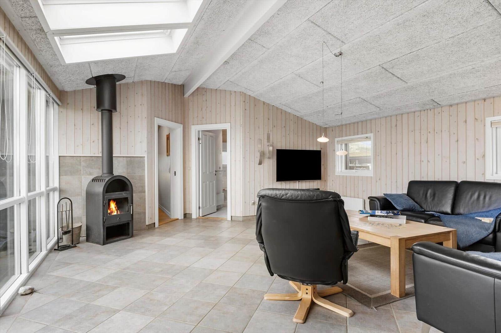 Wohnzimmer mit Kamin, Sofa und Fernseher. Holzwände und Bodenfliesen.