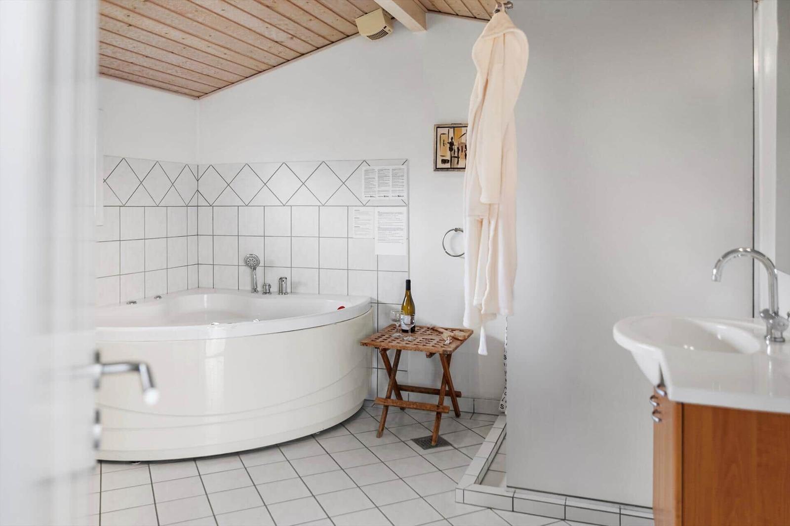 Bad mit Whirlpool, Holzdecke, Bademantel und Waschbecken.