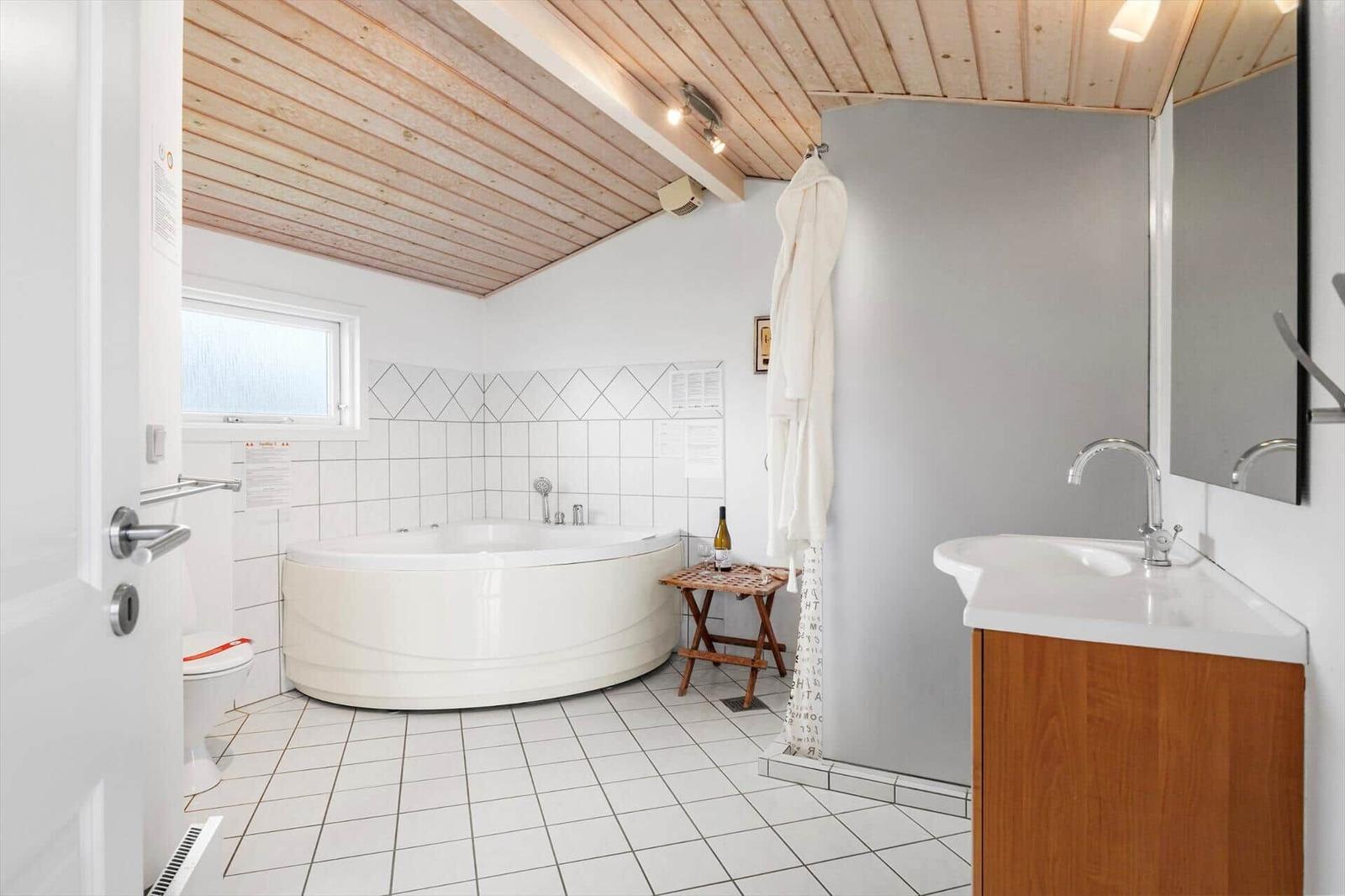 Badezimmer mit Badewanne, Waschbecken und Toilette. Holzdecke und Fliesenboden.